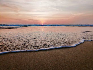 A serene beach at sunset with gentle waves lapping the shore.
