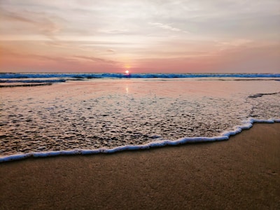 A serene beach at sunset with gentle waves lapping the shore.