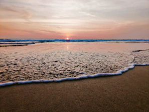 A serene beach at sunset with gentle waves lapping at the shore.