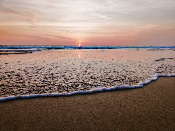 A serene beach at sunset with gentle waves lapping the shore.