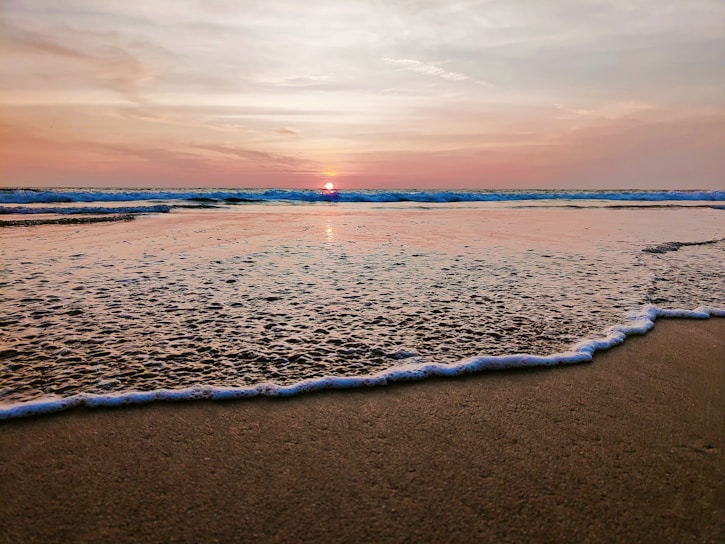A serene beach at sunset with gentle waves lapping the shore.