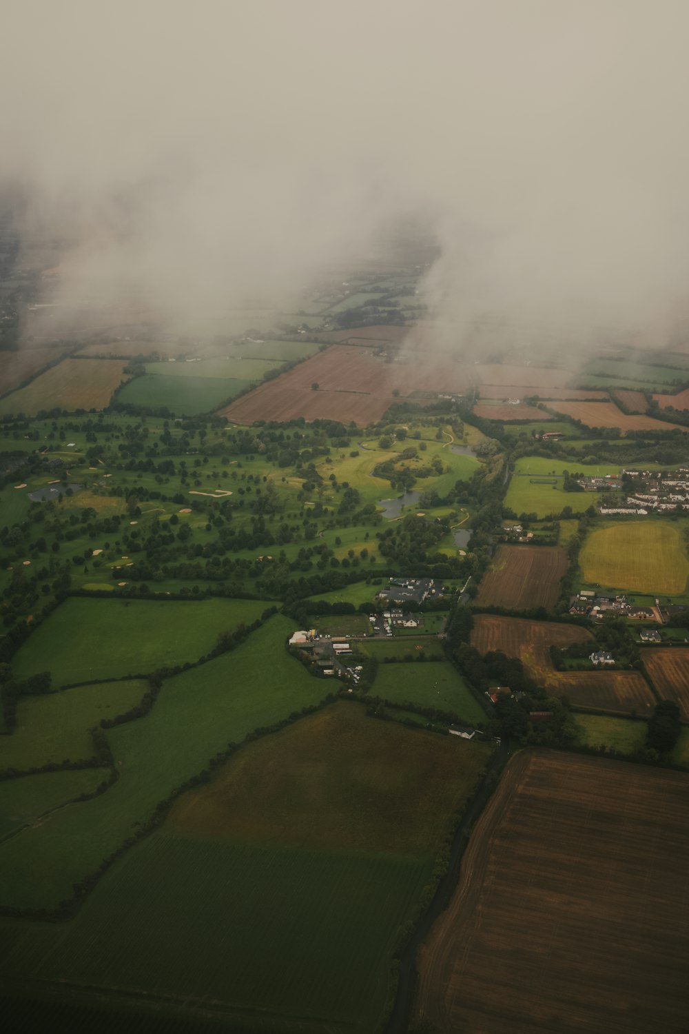 an aerial view of a green field and clouds
