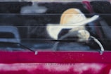 Graffiti art depicting a minimalist portrayal of a person wearing a wide-brimmed hat. The image is spray-painted on a horizontal metal surface, blending stark contrasts of light and dark colors with an abstract style.