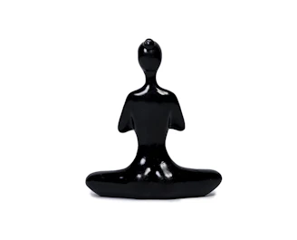 A sleek, minimalist abstract figurine displayed on a wooden desk beside a potted plant.