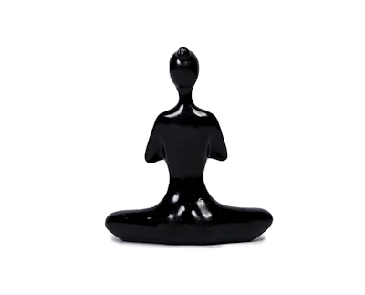 A sleek, minimalist abstract figurine displayed on a wooden desk beside a potted plant.