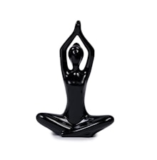 A shiny black sculpture of a human figure in a seated yoga pose, with legs crossed and arms raised above the head, creating a graceful and abstract representation of meditation or tranquility.