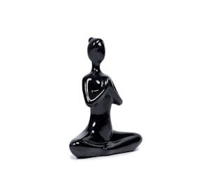 A smooth, black ceramic sculpture depicting a simplified human figure in a meditative, seated pose with an abstract, featureless design.