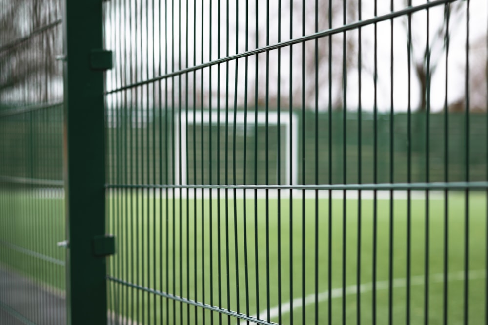 a close up of a fence with a soccer field in the background