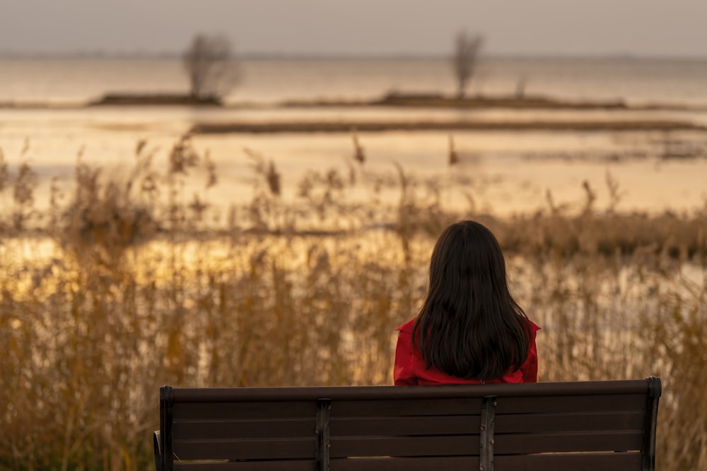 a woman sitting on a bench in front of a body of water