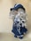 A handcrafted doll with long, curly blonde hair wearing a dark blue, wide-brimmed hat and a matching outfit. The dress is adorned with ribbons and the shoes are also blue. The doll's facial features are delicately embroidered, adding to its charming appearance.