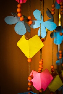 Colorful paper decorations including blue flower shapes and yellow and pink heart shapes are hanging from strings along with orange wooden beads.