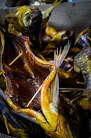 Multiple smoked fish with visible skewers used to hold the fish open, displaying their detailed textures and golden-brown coloration. The fish are arranged closely together, creating a visually dense pattern with overlapping fins and tails.