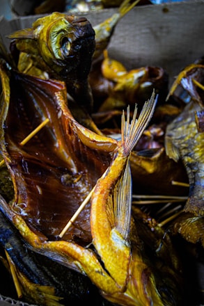 Multiple smoked fish with visible skewers used to hold the fish open, displaying their detailed textures and golden-brown coloration. The fish are arranged closely together, creating a visually dense pattern with overlapping fins and tails.