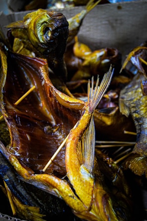 Multiple smoked fish with visible skewers used to hold the fish open, displaying their detailed textures and golden-brown coloration. The fish are arranged closely together, creating a visually dense pattern with overlapping fins and tails.