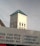 A church tower with a cross on top is visible above a building with a blue roof. In the foreground, there is a partially visible sign featuring text advertising various money transfer services and printing-related activities.