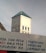 A church tower with a cross on top is visible above a building with a blue roof. In the foreground, there is a partially visible sign featuring text advertising various money transfer services and printing-related activities.