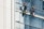 Two workers wearing safety gear are suspended by ropes on the side of a glass building, cleaning the windows. They are equipped with buckets and tools as they perform their task at significant heights.