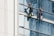 Two workers wearing safety gear are suspended by ropes on the side of a glass building, cleaning the windows. They are equipped with buckets and tools as they perform their task at significant heights.