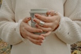 Close-up of a stylish woman’s hand holding a coffee cup, adorned with delicate gold rings.