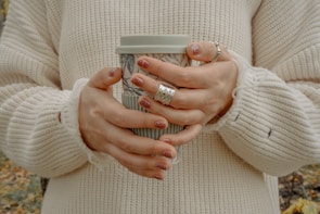 Close-up of a stylish woman’s hand holding a coffee cup, adorned with delicate gold rings.