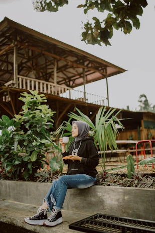A serene woman in a sage green hijab sitting peacefully with a journal and cup of tea.