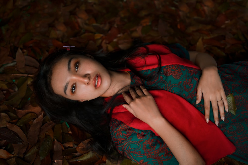 a woman in a red and green dress laying on leaves