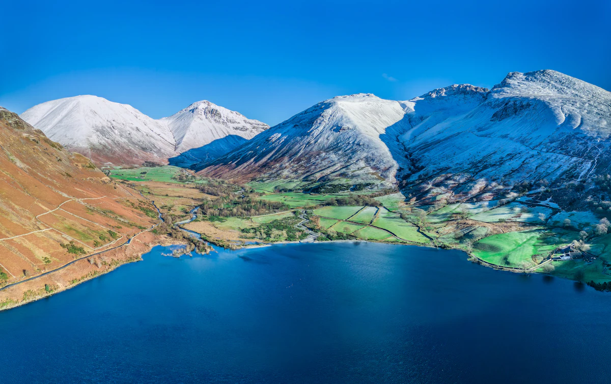 An aerial view of Wast Water and the green fields of Wasdale Head, below fells capped with snow