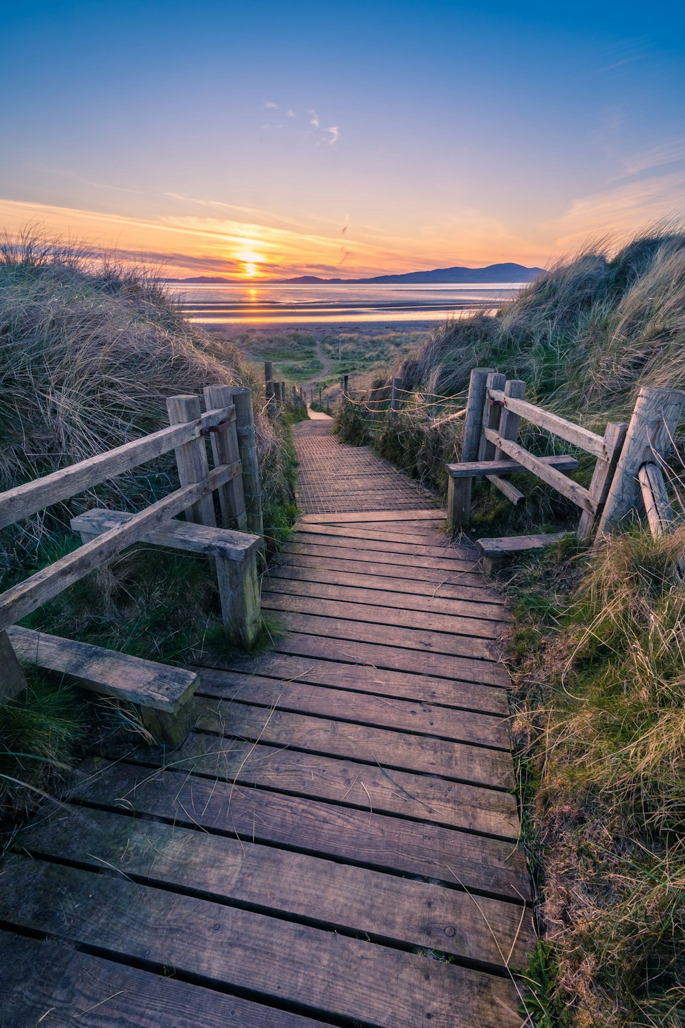 a wooden path leading to the beach at sunset