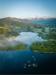 A drone's eye view of a serene lake surrounded by dense forest and distant mountains