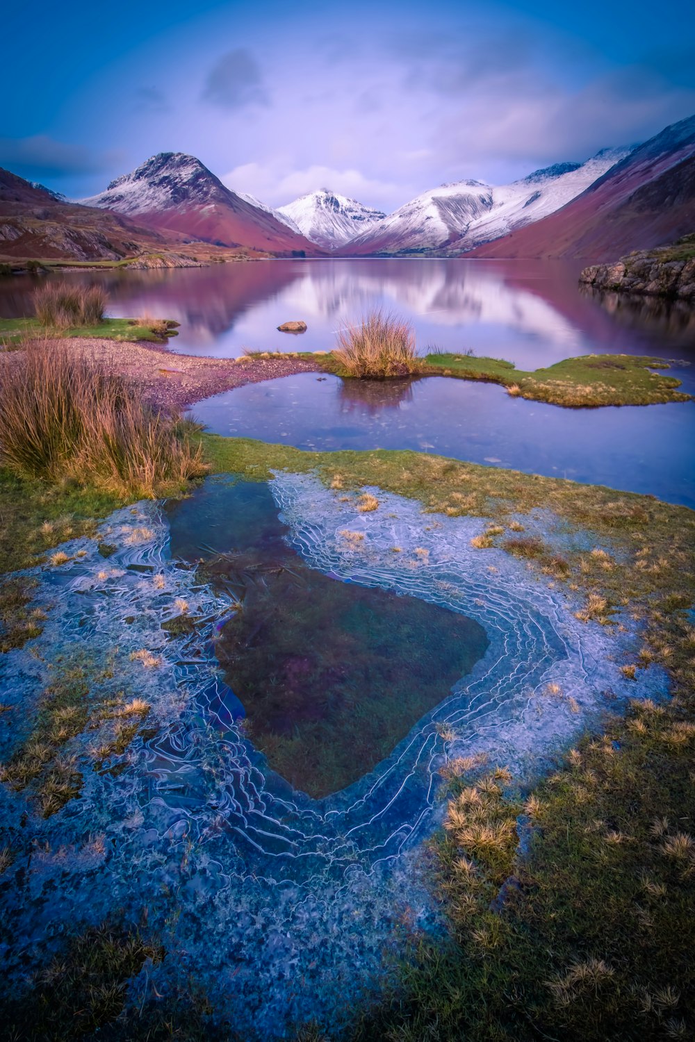 a body of water surrounded by mountains and grass