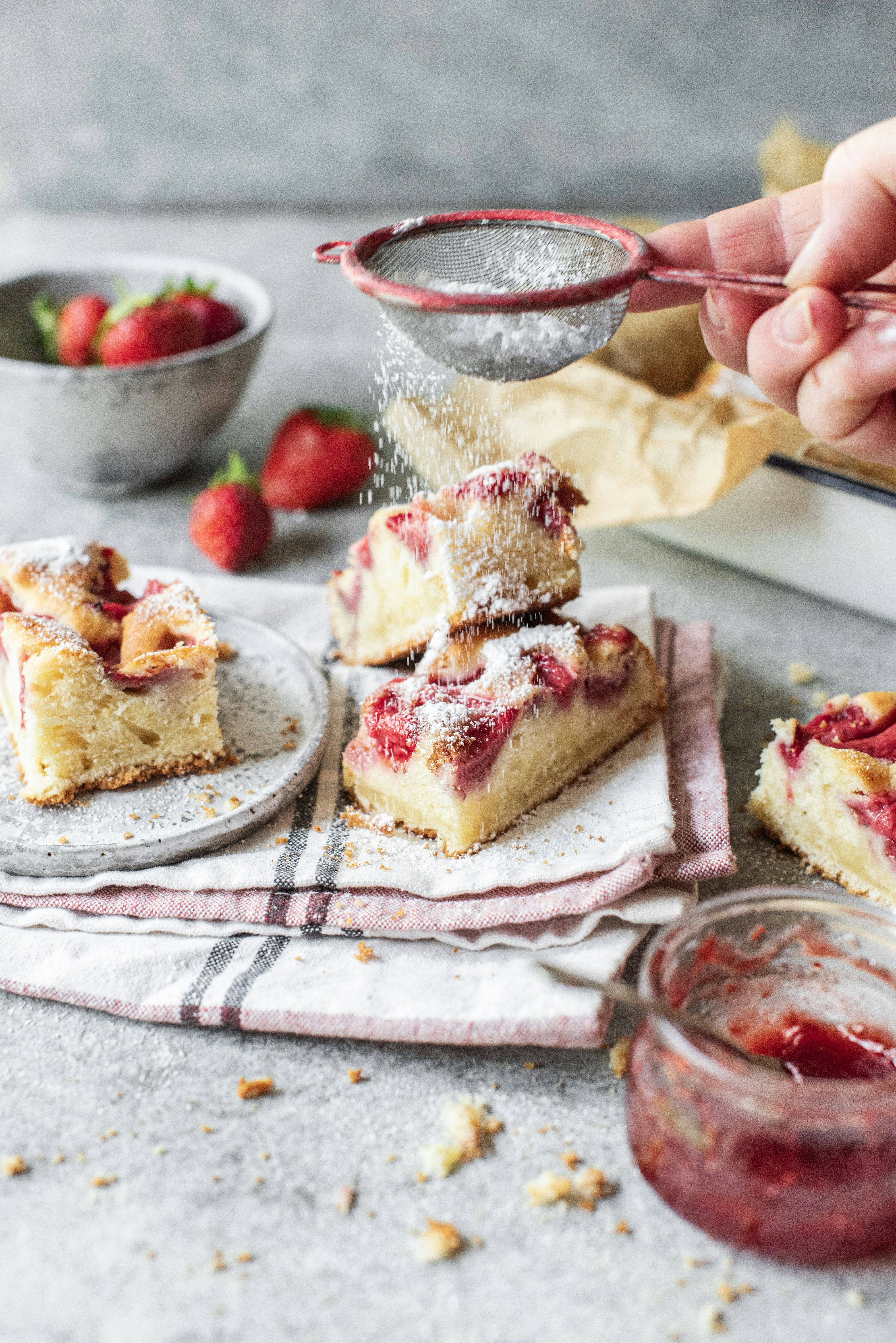 a person sprinkleing strawberries onto a piece of cake