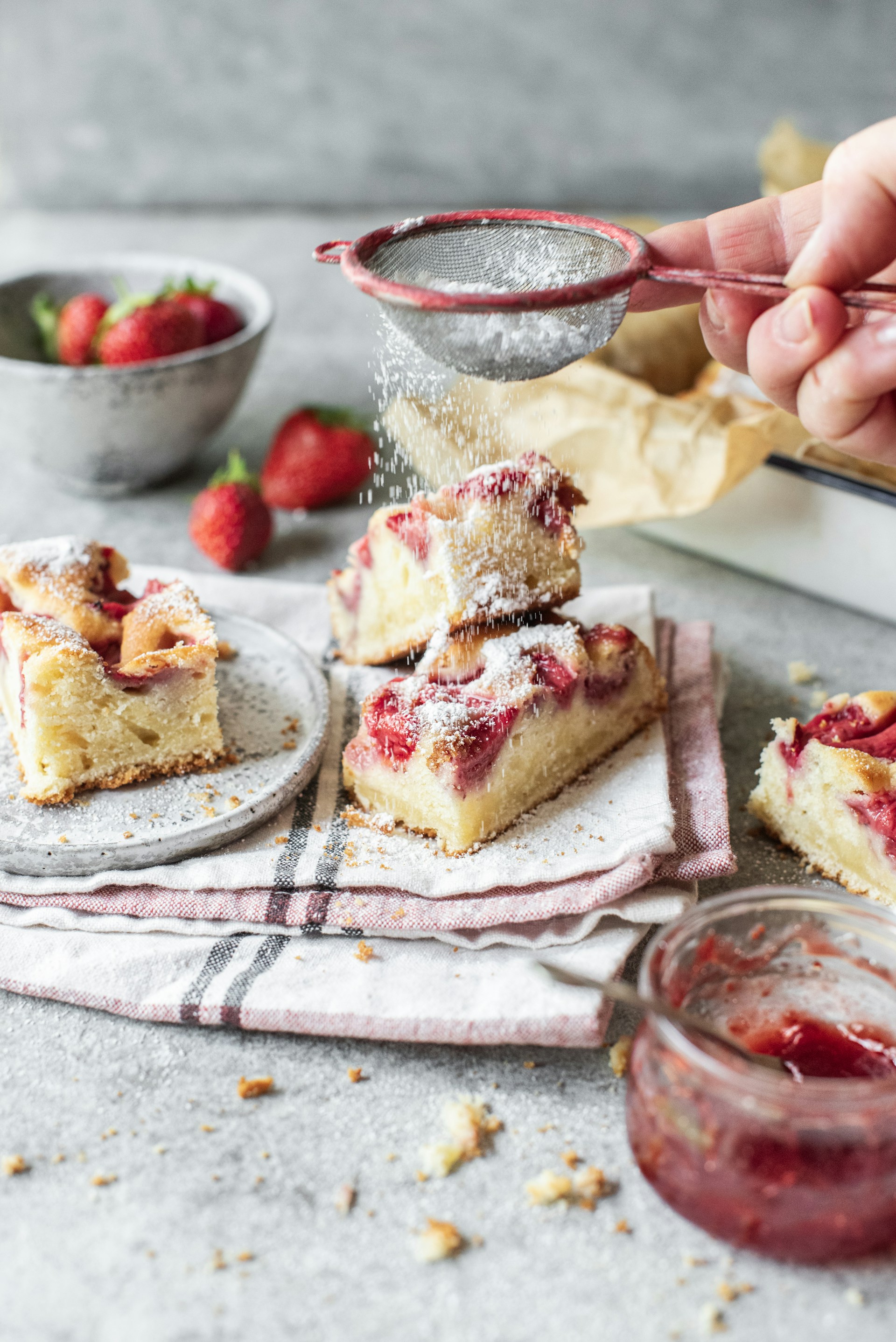 a person sprinkleing strawberries onto a piece of cake