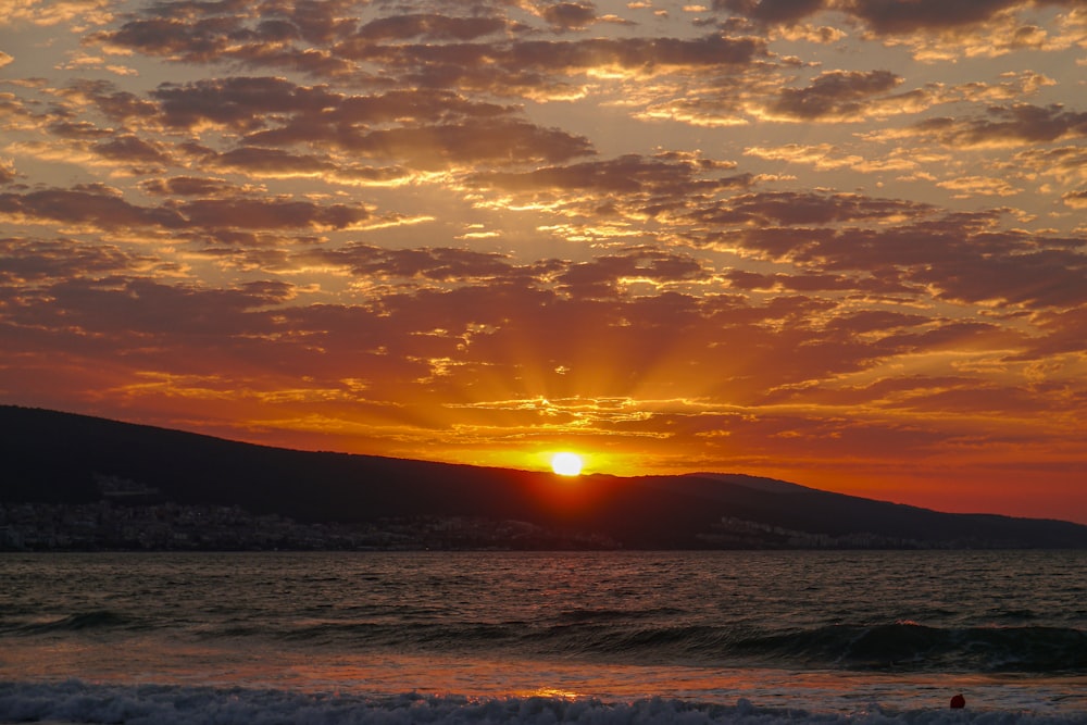 a sunset over a body of water with a mountain in the background