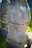A sculpture with intricate carvings displaying abstract and tribal art. The design includes various symbols and patterns, such as spirals and figures, giving an ancient or mystical feel. The sculpture stands in an outdoor setting on a grassy background.