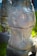 A sculpture with intricate carvings displaying abstract and tribal art. The design includes various symbols and patterns, such as spirals and figures, giving an ancient or mystical feel. The sculpture stands in an outdoor setting on a grassy background.