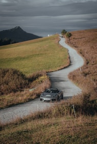 An elegant convertible driving along a mountain road with lush greenery.