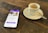 A smartphone displaying a dating app interface is placed on a wooden table next to a small cup of espresso on a saucer with a spoon.