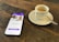 A smartphone displaying a dating app interface is placed on a wooden table next to a small cup of espresso on a saucer with a spoon.