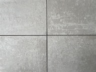 Four square cement tiles arranged in a grid pattern with visible seams between them. The surface of each tile has a textured, speckled appearance with shades of gray and subtle variations in tone.