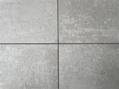 Four square cement tiles arranged in a grid pattern with visible seams between them. The surface of each tile has a textured, speckled appearance with shades of gray and subtle variations in tone.