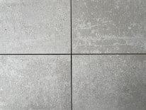 Four square cement tiles arranged in a grid pattern with visible seams between them. The surface of each tile has a textured, speckled appearance with shades of gray and subtle variations in tone.