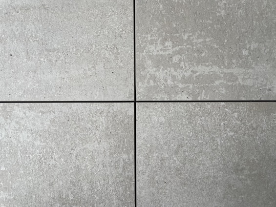Four square cement tiles arranged in a grid pattern with visible seams between them. The surface of each tile has a textured, speckled appearance with shades of gray and subtle variations in tone.