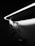 A black and white photograph shows a sleek, modern closet area with wooden hangers hanging on a metallic rod. Above, an elegantly curved LED light casts a soft glow and illuminates the space, creating contrasting shadows on the wall.