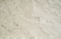 A close-up view of a smooth, creamy beige marble surface featuring intricate patterns and natural veining that give it a luxurious appearance.