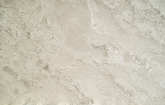 A close-up view of a smooth, creamy beige marble surface featuring intricate patterns and natural veining that give it a luxurious appearance.