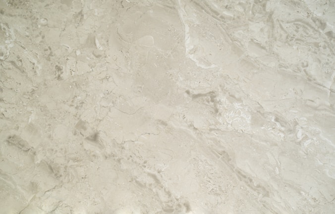 A close-up view of a smooth, creamy beige marble surface featuring intricate patterns and natural veining that give it a luxurious appearance.