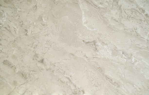 A close-up view of a smooth, creamy beige marble surface featuring intricate patterns and natural veining that give it a luxurious appearance.