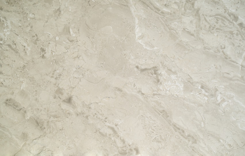 A close-up view of a smooth, creamy beige marble surface featuring intricate patterns and natural veining that give it a luxurious appearance.