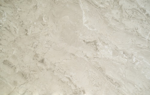 A close-up view of a smooth, creamy beige marble surface featuring intricate patterns and natural veining that give it a luxurious appearance.