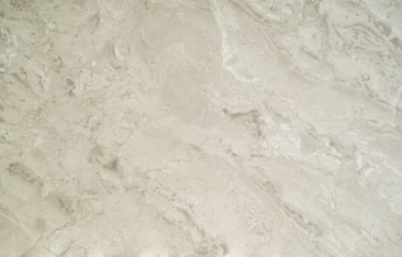 A close-up view of a smooth, creamy beige marble surface featuring intricate patterns and natural veining that give it a luxurious appearance.